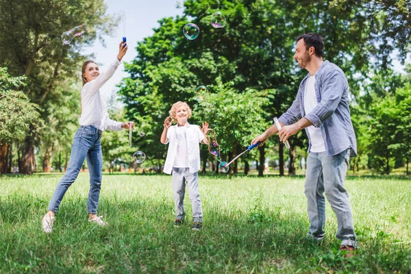 Mère, père et fils en vêtements décontractés jouant avec des bulles de savon dans le parc — Photo de stock