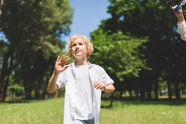 Adorable garçon en blanc Gesturing près de bulles de savon dans le parc — Photo de stock