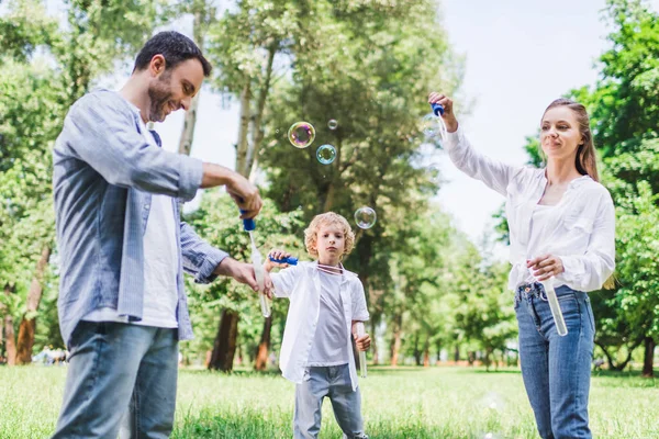 Красивая мать, отец и сын играют с мыльными пузырями в парке — стоковое фото