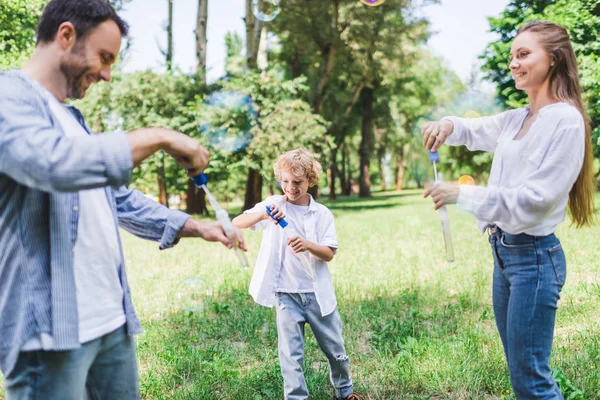 Bella madre, padre e figlio giocare con bolle di sapone nel parco — Foto stock