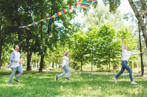 Excited family running and playing with flying kite in park during daytime — Stock Photo