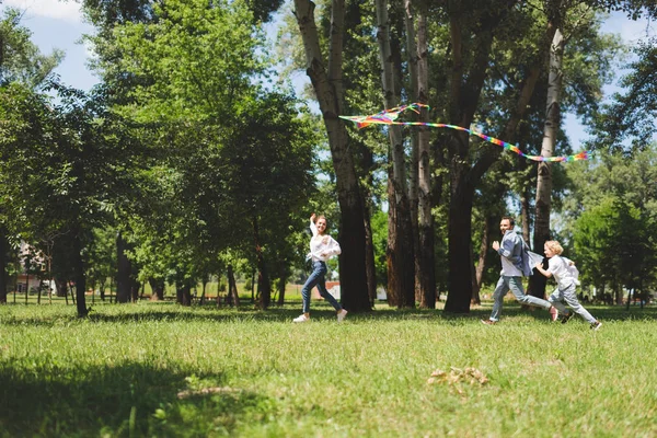 Aufgeregte Familie rennt und spielt mit fliegendem Drachen im Park — Stockfoto