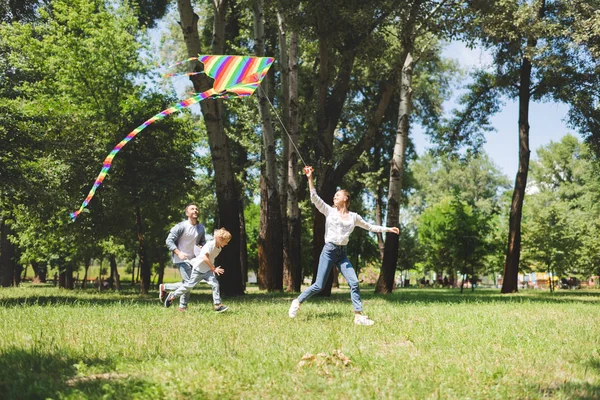 Família animada correndo e brincando com pipa voadora no parque — Fotografia de Stock