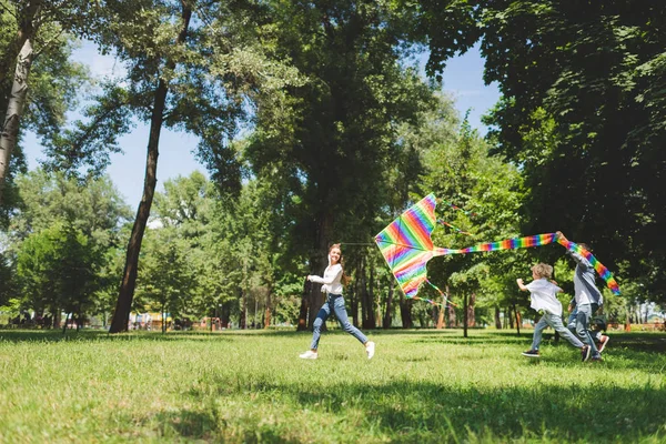 Glückliche Familie läuft und spielt mit fliegendem Drachen im Park mit Kopierraum — Stockfoto