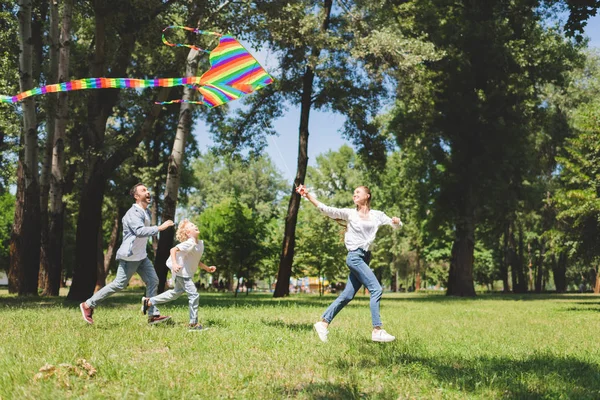 Glücklich Familie läuft und spielt mit bunten fliegenden Drachen im Park — Stockfoto