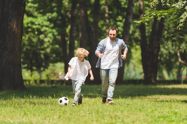 Отец и очаровательный сын играют в футбол в парке вместе — стоковое фото