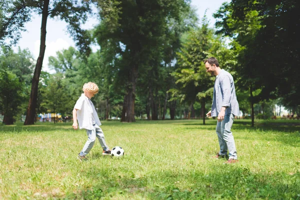 Padre y adorable hijo jugando al fútbol en el parque juntos - foto de stock