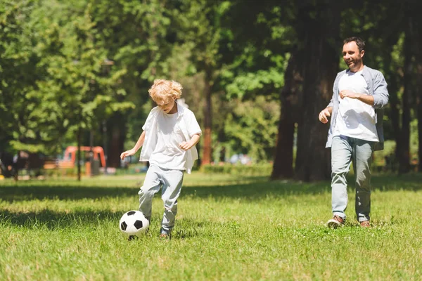 Vater und entzückender Sohn spielen tagsüber Fußball im Park — Stockfoto