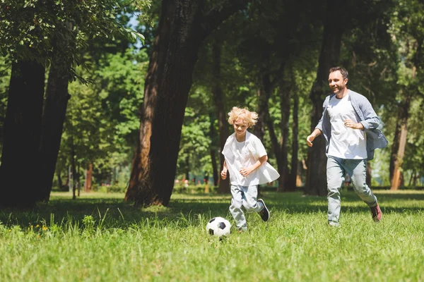 Padre y adorable hijo jugando fútbol con pelota de fútbol en el parque con espacio de copia - foto de stock