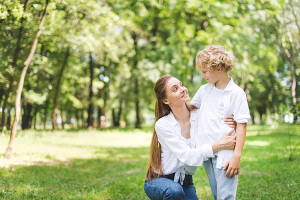 Красива усміхнена мама обіймає сина в парку вдень — стокове фото