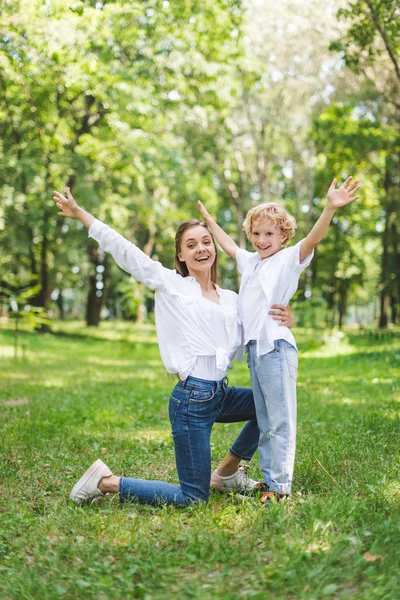 Schöne lächelnde Mutter und Sohn mit erhobenen Händen im Park, die in die Kamera schauen — Stockfoto