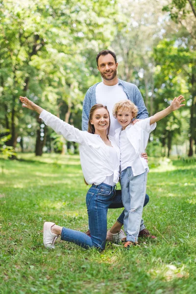 Счастливая семья с протянутыми руками, смотрящая на камеру в парке — стоковое фото