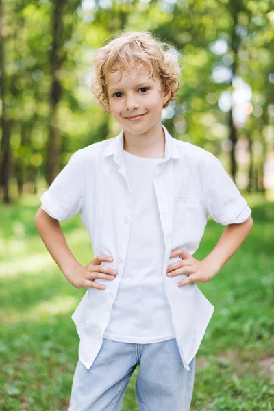 Cute happy boy with Hands On Hips in park looking at camera — Stock Photo