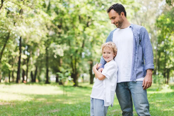 Handsome father hugging adorable son in park with copy space — Stock Photo