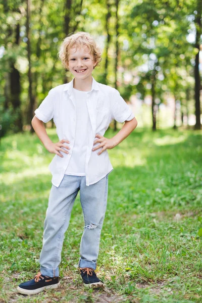 Carino ragazzo felice con le mani sui fianchi nel parco guardando la fotocamera — Foto stock