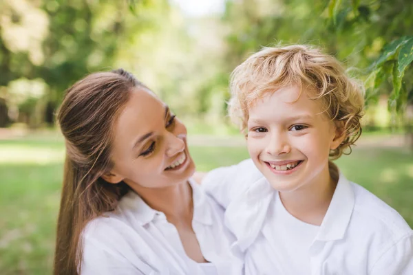 Beautiful mother with happy adorable son looking at camera in park — Stock Photo