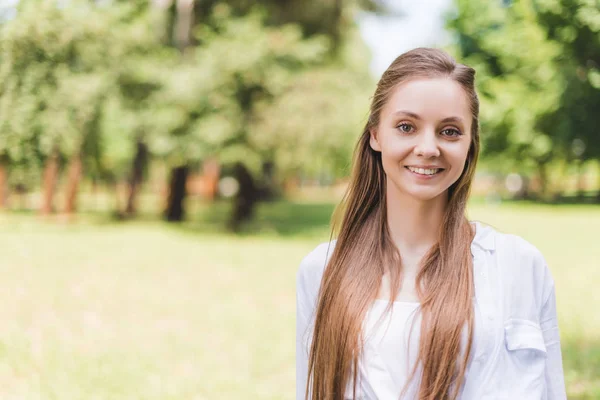 Selective focus of beautiful smiling woman in park looking at camera — Stock Photo