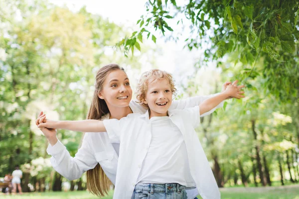 Красивая счастливая мать держась за руки с очаровательным сыном в парке — стоковое фото