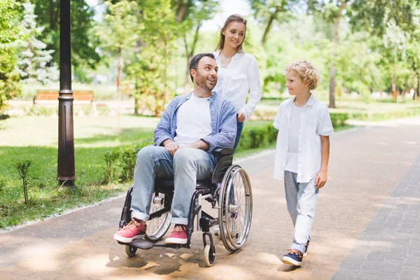 Madre e hijo adorable con padre discapacitado en silla de ruedas en el parque - foto de stock