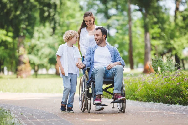 Belle mère roulant en fauteuil roulant avec père handicapé dans le parc près du fils — Photo de stock