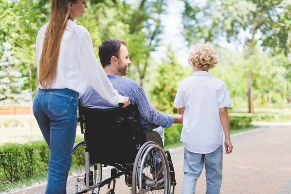 Vista trasera de la madre silla de ruedas rodante con padre discapacitado en el parque - foto de stock