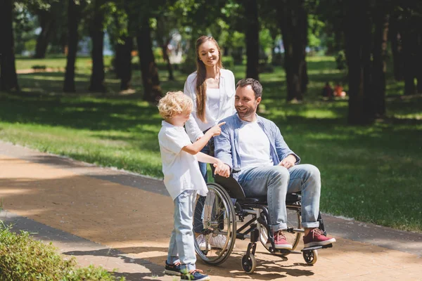 Hermosa madre e hijo con padre discapacitado en silla de ruedas en el parque - foto de stock