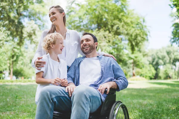 Famille heureuse avec père handicapé en fauteuil roulant dans le parc — Photo de stock