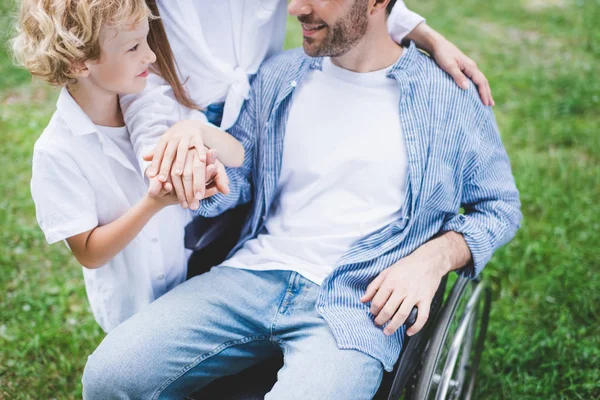 Vue recadrée de la mère et du fils avec un père handicapé en fauteuil roulant dans le parc — Photo de stock