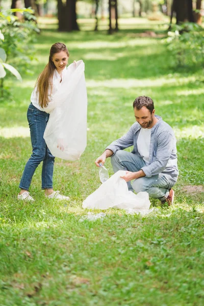 Homme et femme ramasser les ordures dans des sacs en plastique dans le parc — Photo de stock