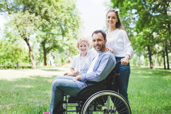 Felice madre e figlio con padre disabile sulla sedia a rotelle nel parco — Foto stock