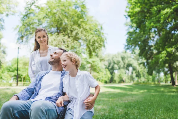 Feliz madre e hijo con padre discapacitado en silla de ruedas en el parque - foto de stock