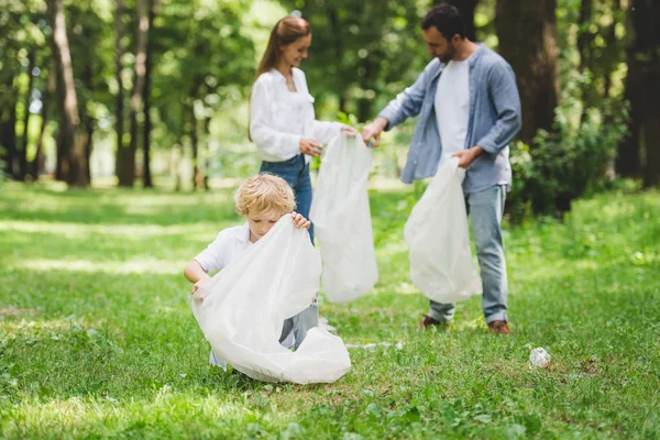 Familia recogiendo basura en bolsas de plástico en el parque - foto de stock