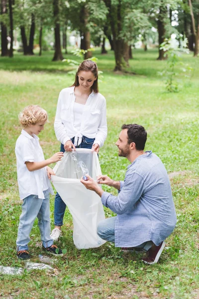 Família feliz pegando lixo no saco de plástico no parque — Fotografia de Stock