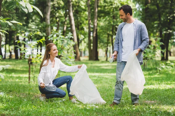 Uomo e bella donna che raccolgono spazzatura in sacchetti di plastica nel parco — Foto stock