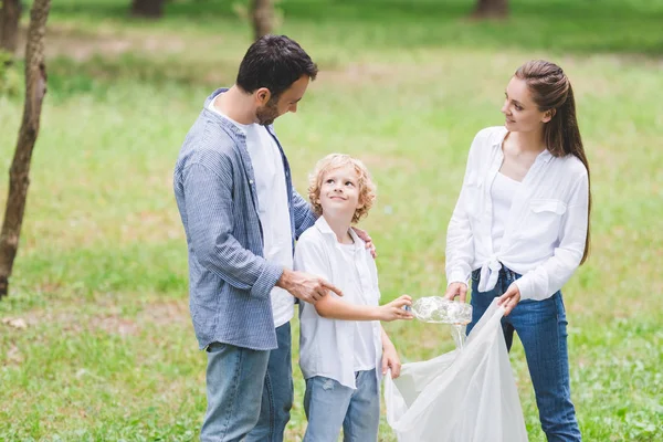 Familia en ropa casual recogiendo basura en bolsa de plástico en el parque - foto de stock