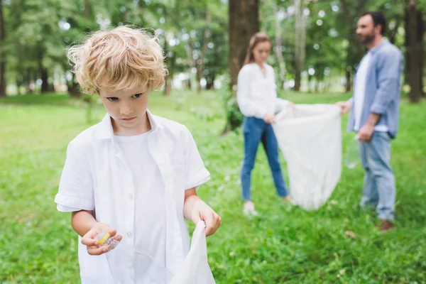 Messa a fuoco selettiva del ragazzo mettere immondizia in sacchetto di plastica nel parco — Foto stock