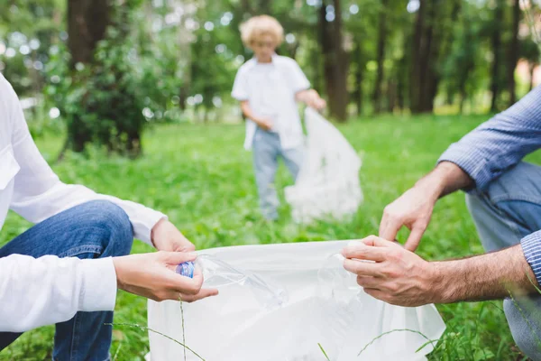 Partial view of family picking up garbage in plastic bag in park — Stock Photo