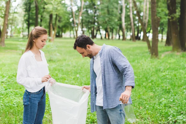 Uomo e bella donna che raccolgono spazzatura in sacchetto di plastica nel parco — Foto stock