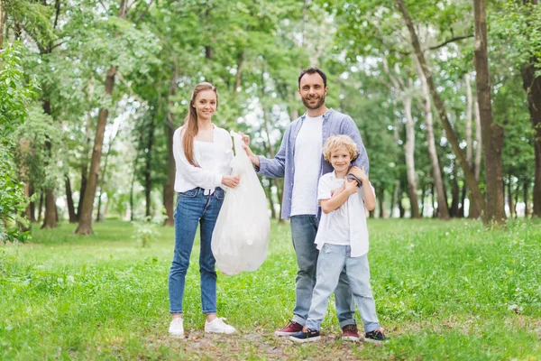 Padre, madre e hijo con basura en bolsa de plástico en el parque - foto de stock