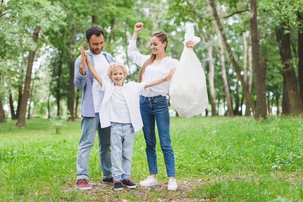 Feliz padre, madre e hijo con bolsa de basura de plástico en el parque - foto de stock