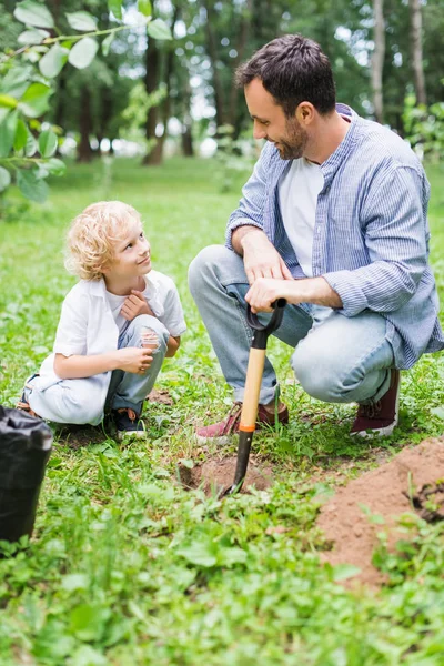 Padre e hijo lindo durante la excavación de suelo con pala para plantar plántulas en el parque - foto de stock