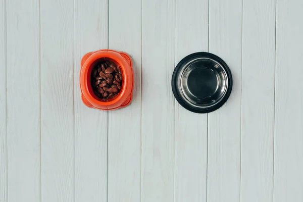 Верхний вид миски с кормом для домашних животных и пустой миской на деревянной поверхности с копировальным пространством — стоковое фото