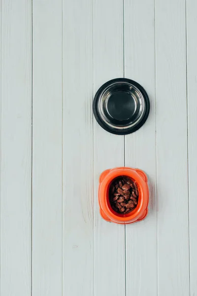 Vista superior da tigela com alimentos para animais de estimação e tigela vazia na superfície de madeira — Fotografia de Stock