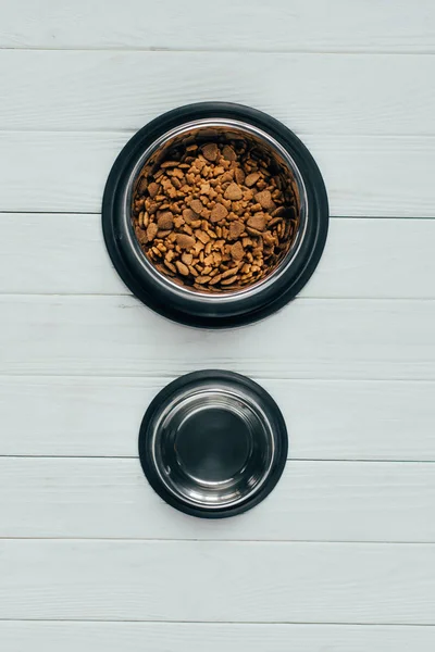 Vista superior da tigela com alimentos para animais de estimação e tigela vazia na superfície de madeira — Fotografia de Stock