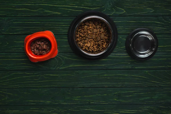 Top view of bowls with pet food in row on green wooden surface — Stock Photo