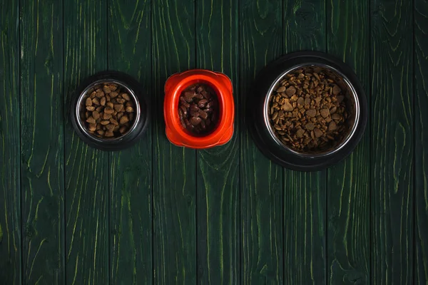 Top view of bowls with pet food in row on green wooden surface with copy space — Stock Photo