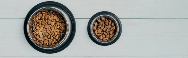 Colpo panoramico di ciotole con cibo per animali su superficie di legno bianca — Foto stock