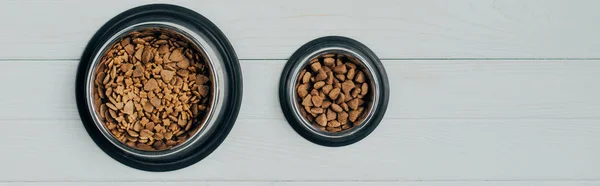 Panoramic shot of bowls with pet food on white wooden surface — Stock Photo