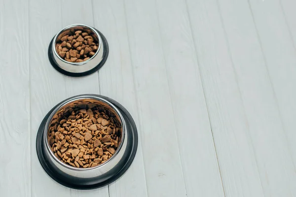 Metal bowls with pet food on white wooden surface — Stock Photo