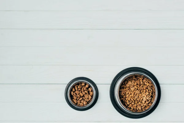 Vue de dessus des bols avec nourriture pour animaux de compagnie sur la surface en bois blanc — Photo de stock